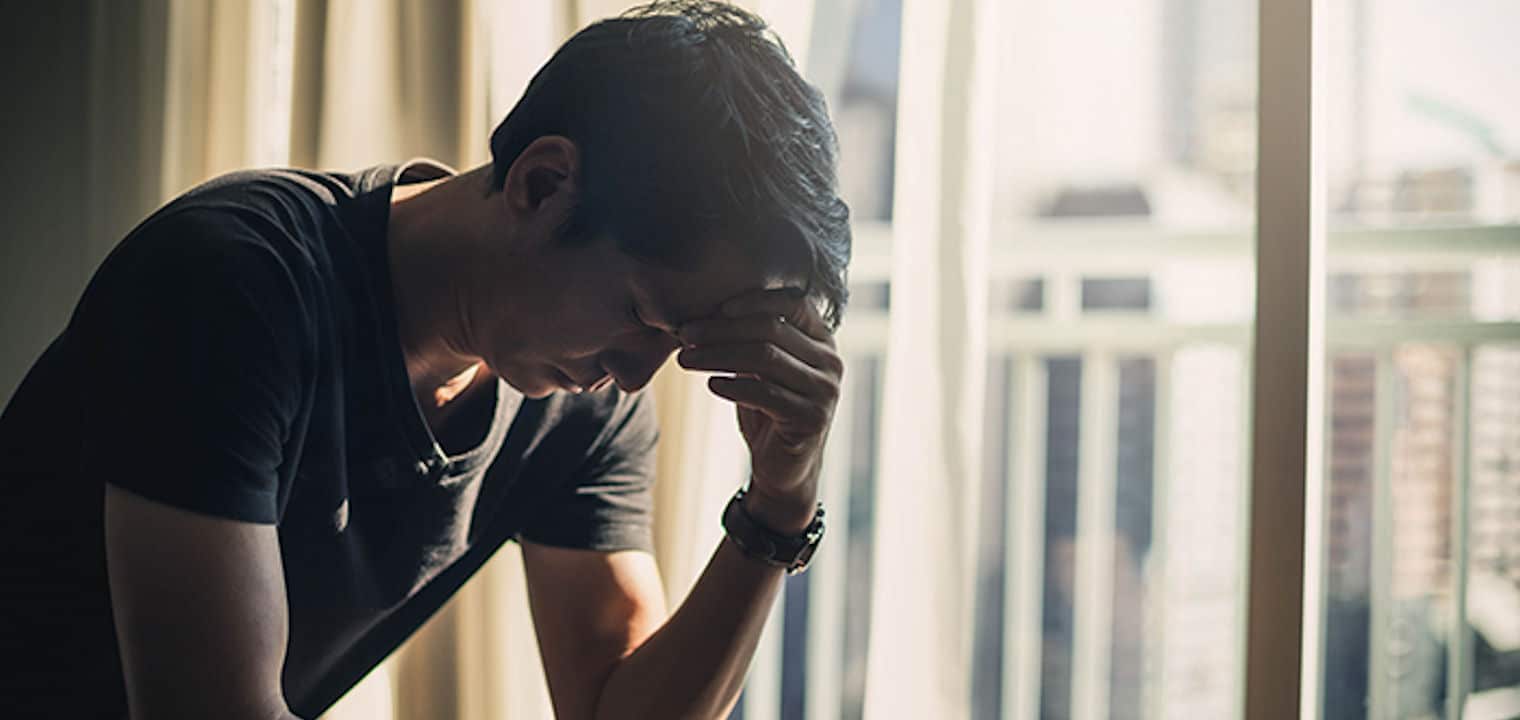 Upset man holding head in front of closed window