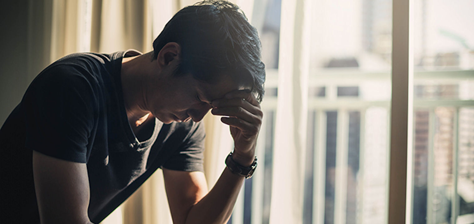 Man-with-watch-holding-his-head-in-dark-apartment