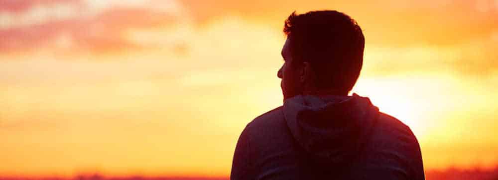 Rear view of a man wearing a hoodie while watching the sun set over a flat landscape