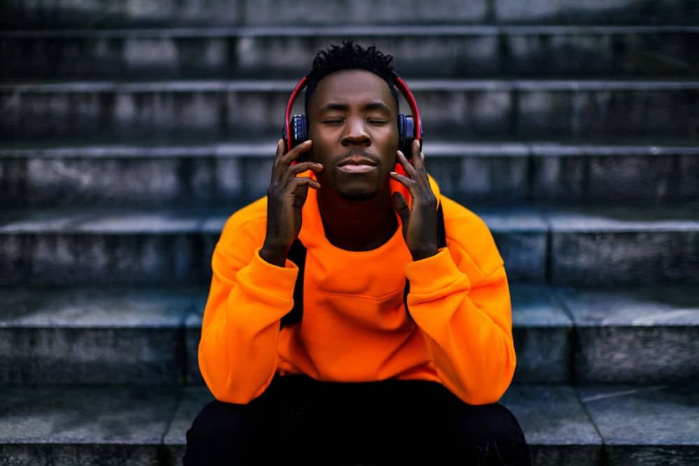 Man relaxing on stairs with eyes closed, holding cans-style headphones against his earls