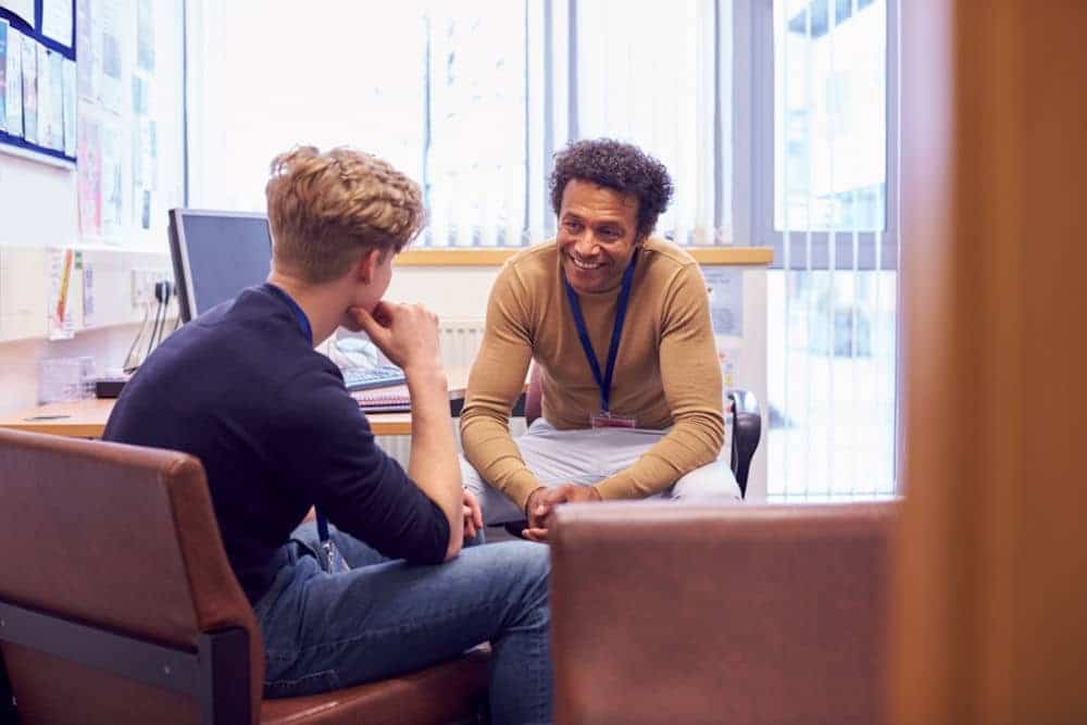 Therapist leaning over desk to reassure teenage boy about bigorexia